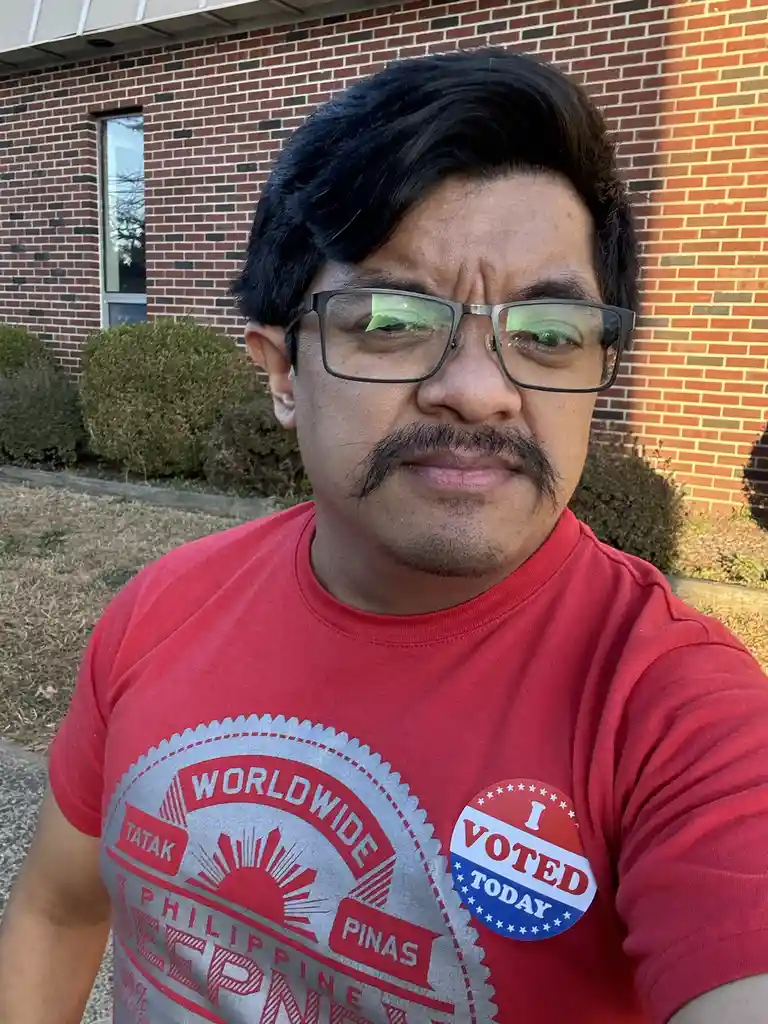 A man with dark hair, glasses, and a mustache wears a red t-shirt with a 'WORLDWIDE TATAK PINAS PHILIPPINE' graphic and an…