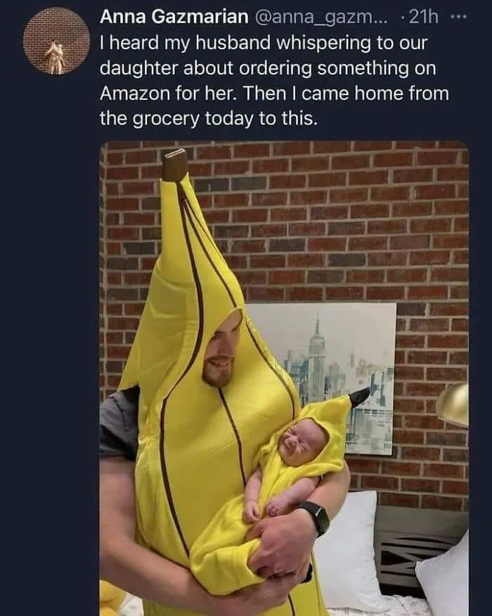 A man in a large, yellow banana costume is holding a baby also dressed in a smaller banana costume. The baby has a…