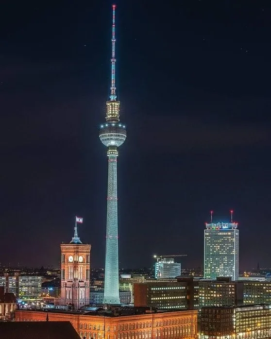 A nighttime cityscape photo of Berlin's iconic Fernsehturm (TV Tower) illuminated against a dark sky, with surrounding…