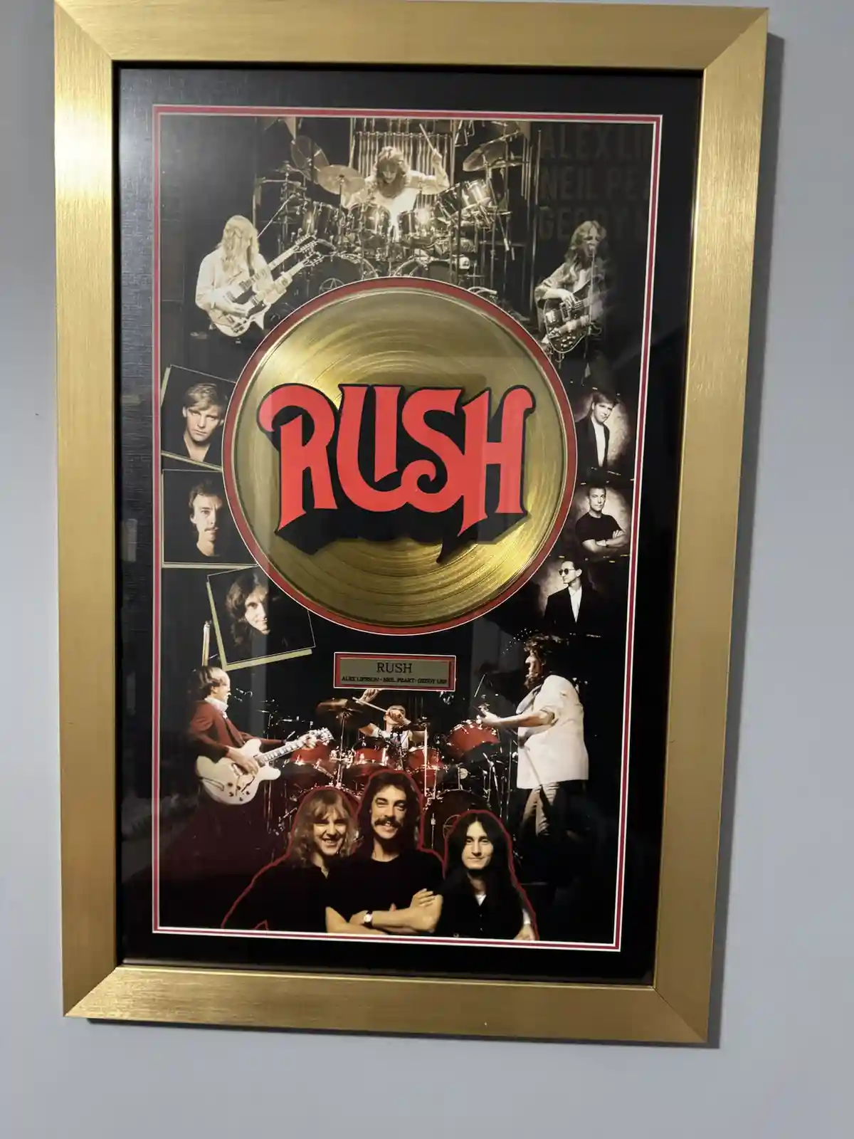 A framed gold record for the band Rush, featuring the band's logo in red, surrounded by various photos of the band members…
