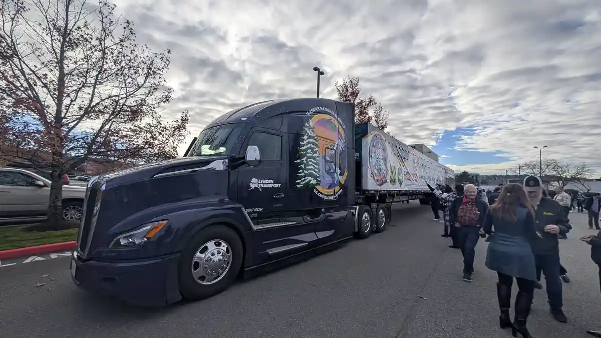 A large black semi-truck with 'Lynden Transport' and 'U.S. Capitol Christmas Tree' branding is parked outdoors, its trailer…