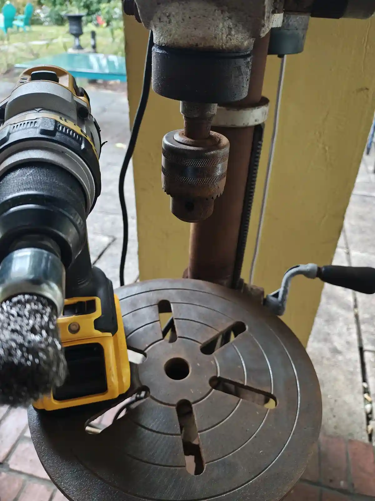 A yellow and black power drill with a wire brush attachment is positioned next to a rusty, old-fashioned drill press on a…
