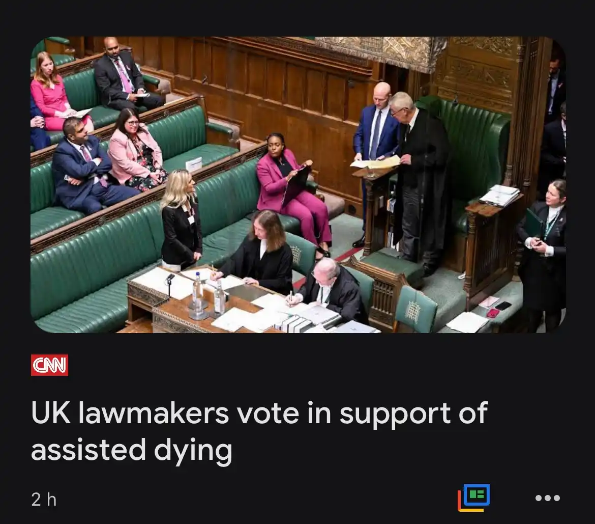 A photo from the UK Parliament shows lawmakers seated in green leather benches during a formal session. Two men stand at a…