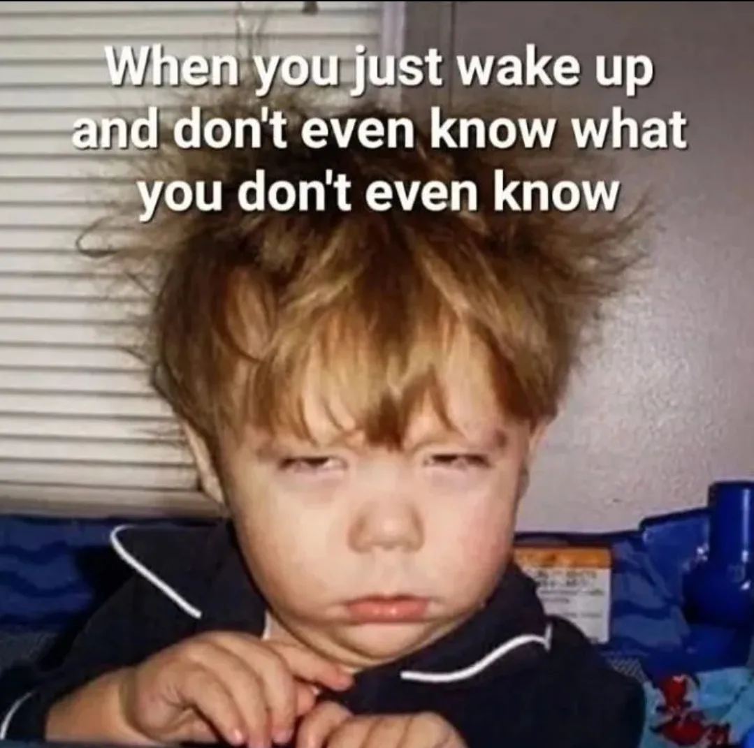 A young child with messy, spiky hair and a dazed, confused expression looks directly at the camera while wearing a dark blue…