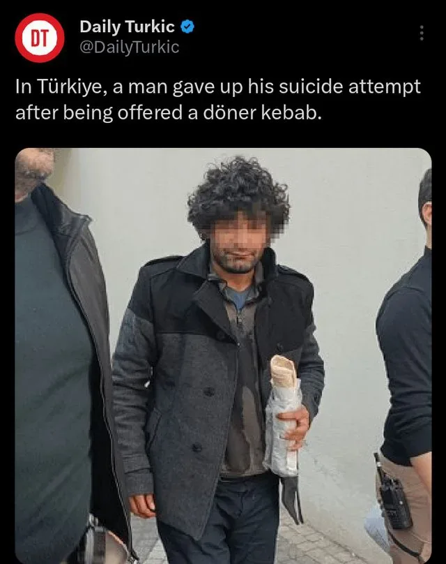 A man with curly dark hair and a beard, wearing a dark grey and black coat, is holding a wrapped döner kebab. He is flanked…
