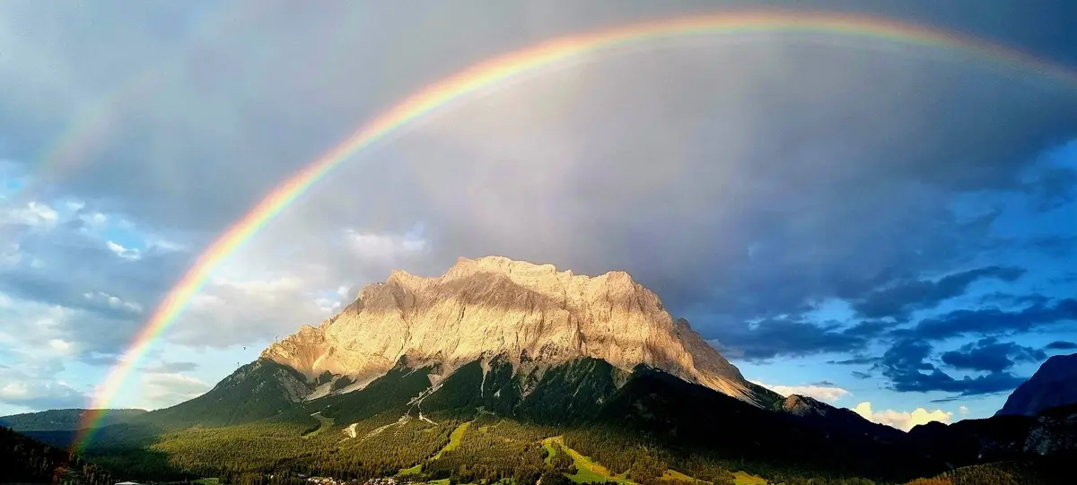 A majestic mountain range under a dramatic sky with a vivid, full rainbow arching over it. The overlaid text reads 'i'm not…