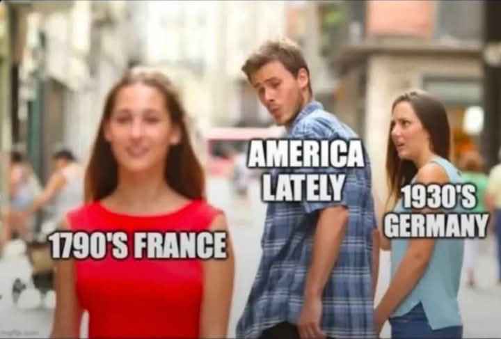A man in a plaid shirt stands in a street, looking away from a blurred woman in a red dress labeled '1790'S FRANCE' and…