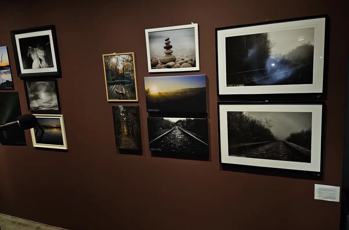 A wall displays multiple framed photographs of nature scenes including stacked stones, train tracks, forests, and sunrises…