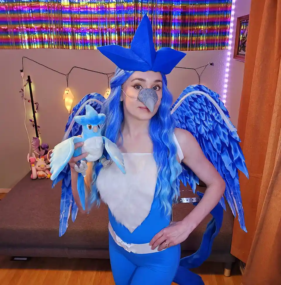 A person dressed in a detailed blue and white costume resembling the Pokémon Articuno, complete with a large blue headpiece…