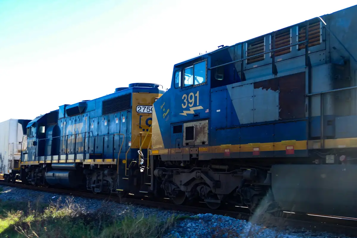 Two blue and yellow CSX freight locomotives, numbered 2750 and 391, are coupled together on railway tracks under a bright…