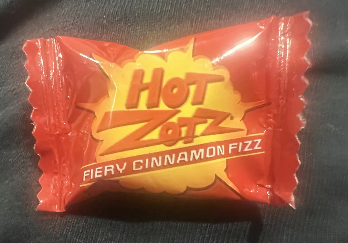 A close-up photo of a single Hot Zotz candy wrapper, which is red and yellow with the brand name and flavor 'Fiery Cinnamon…