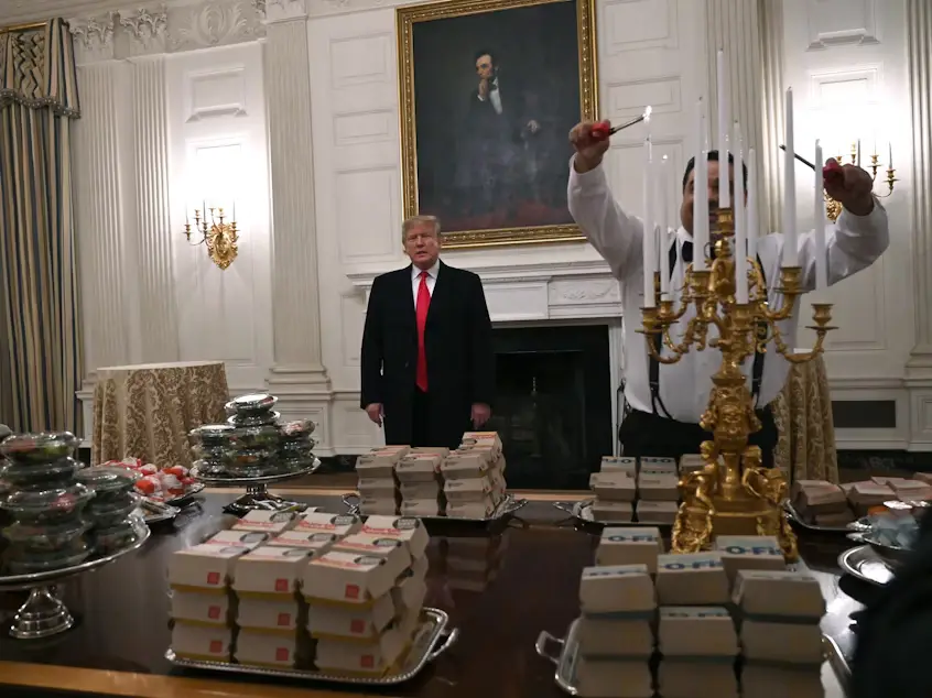 a man in a white shirt and black suspenders stands behind a table full of stacks of boxes labeled 'O-FR' and a large ornate…
