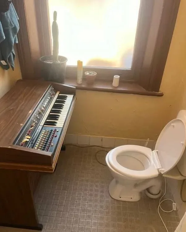A bathroom with a white toilet on the right and a large, wooden, vintage-style organ on the left, both situated on a tiled…