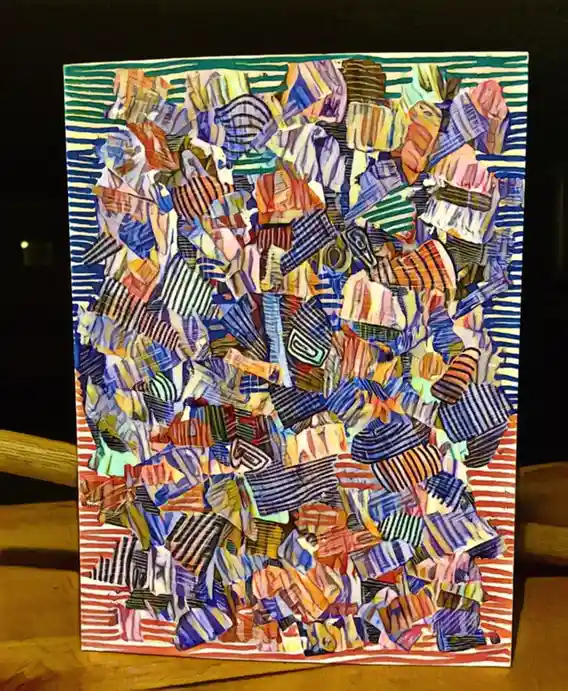 A colorful, abstract artwork made of layered, torn paper pieces with various stripes and patterns, framed and standing…
