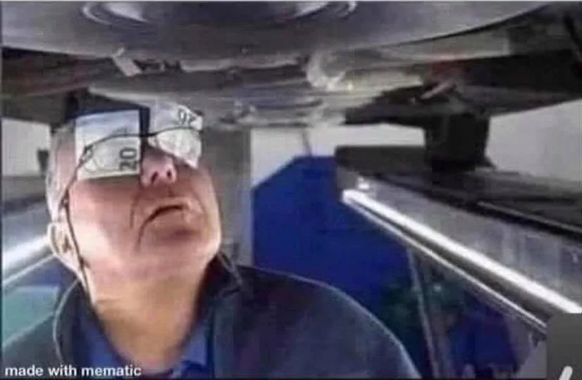 A man with two $20 bills taped over his eyes is looking up at the underside of a vehicle. The overlaid text reads 'i'm not…