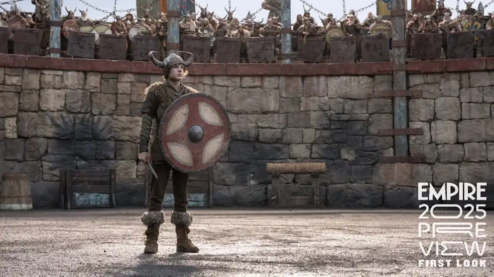 A young Viking warrior in horned helmet and fur-trimmed boots stands alone in front of a stone wall, holding a round shield…
