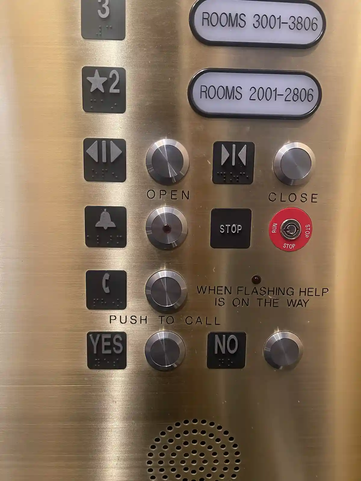 A close-up of a hotel elevator control panel with buttons for floors, open/close, stop, and a red emergency stop button…
