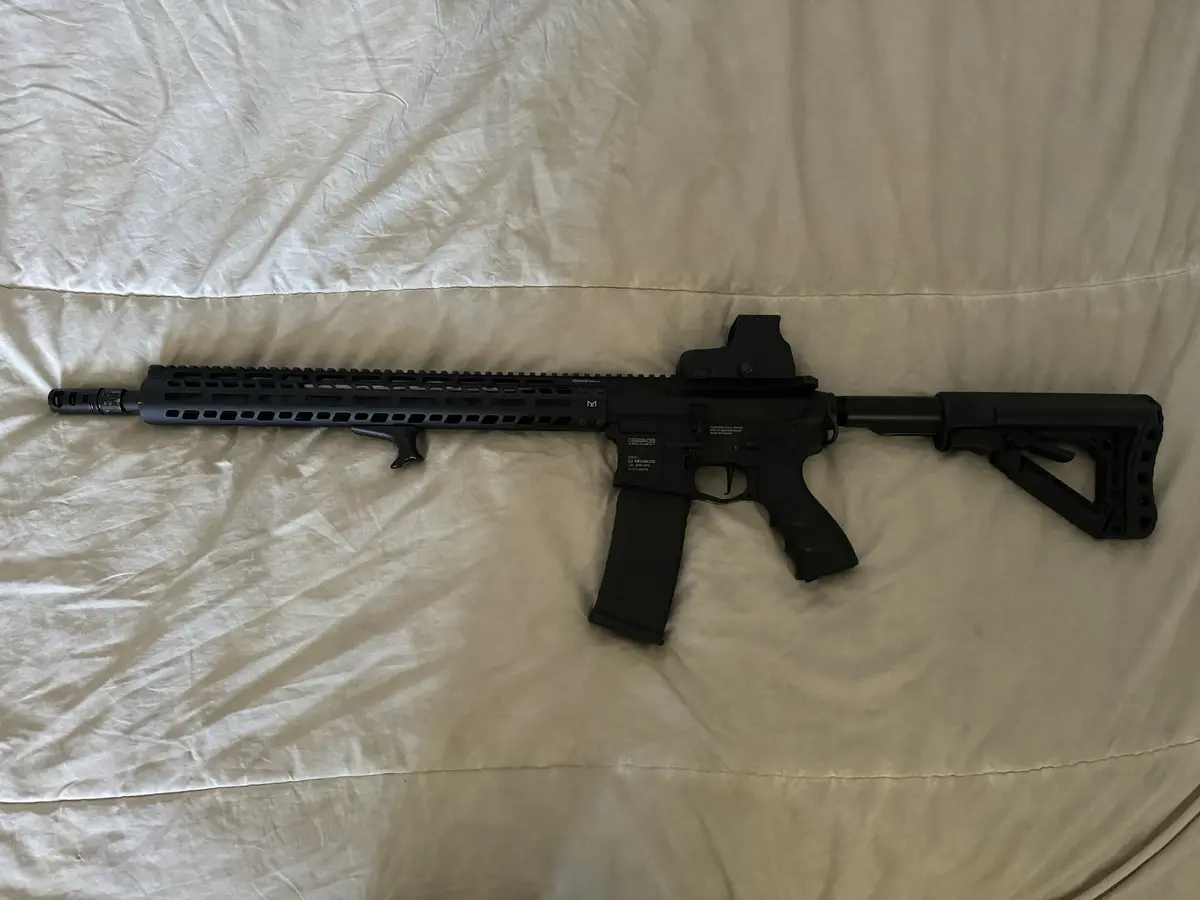 A black rifle with a scope and stock lies horizontally on a wrinkled white sheet. Overlaid text reads 'i just got my new…