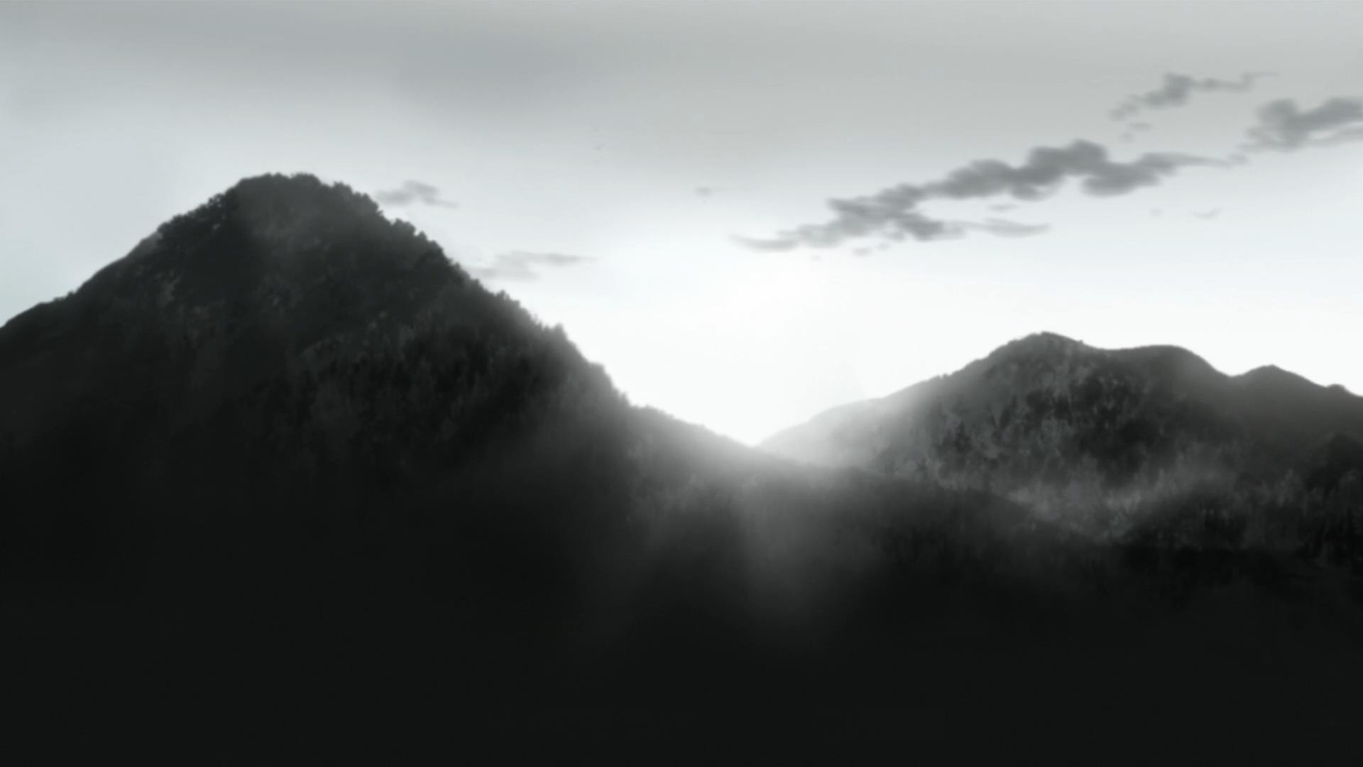 A black-and-white image of misty mountains with a bright sun breaking through the clouds between two peaks. The overlaid…