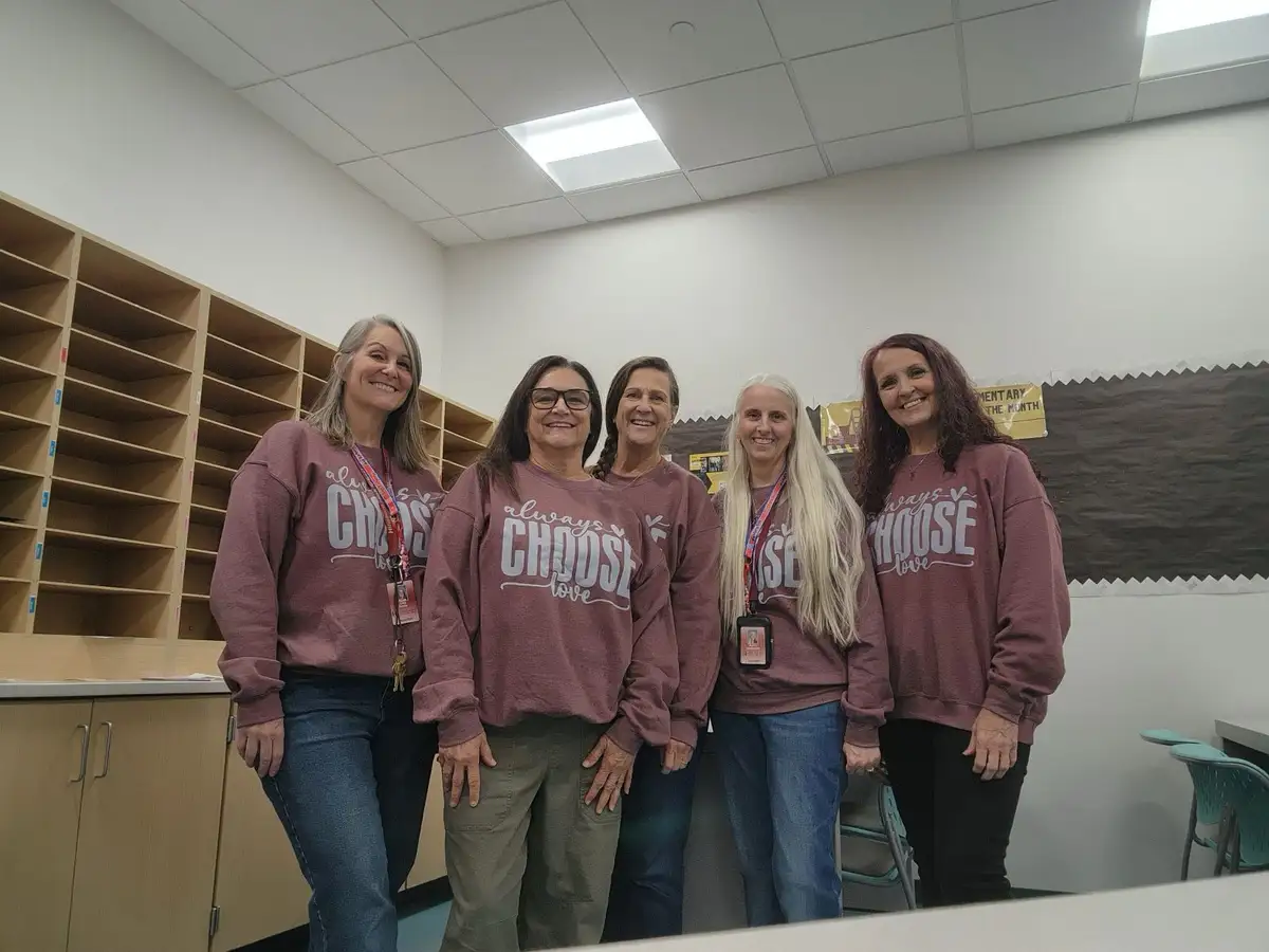 Five smiling women in matching maroon sweatshirts with the phrase 'always choose love' printed in white stand together in…