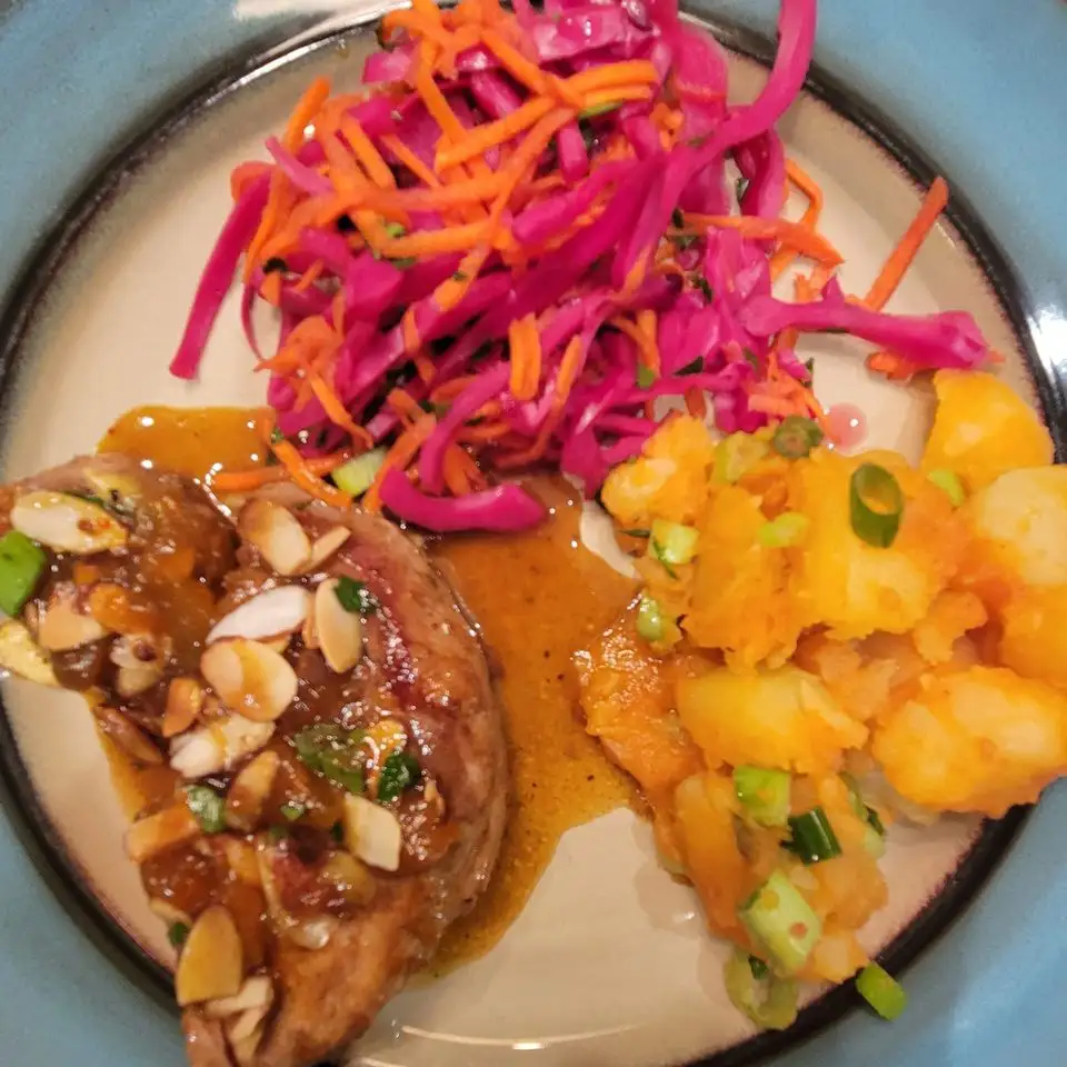 A close-up photo of a plated meal featuring a glazed meat dish topped with sliced almonds and green onions, accompanied by…