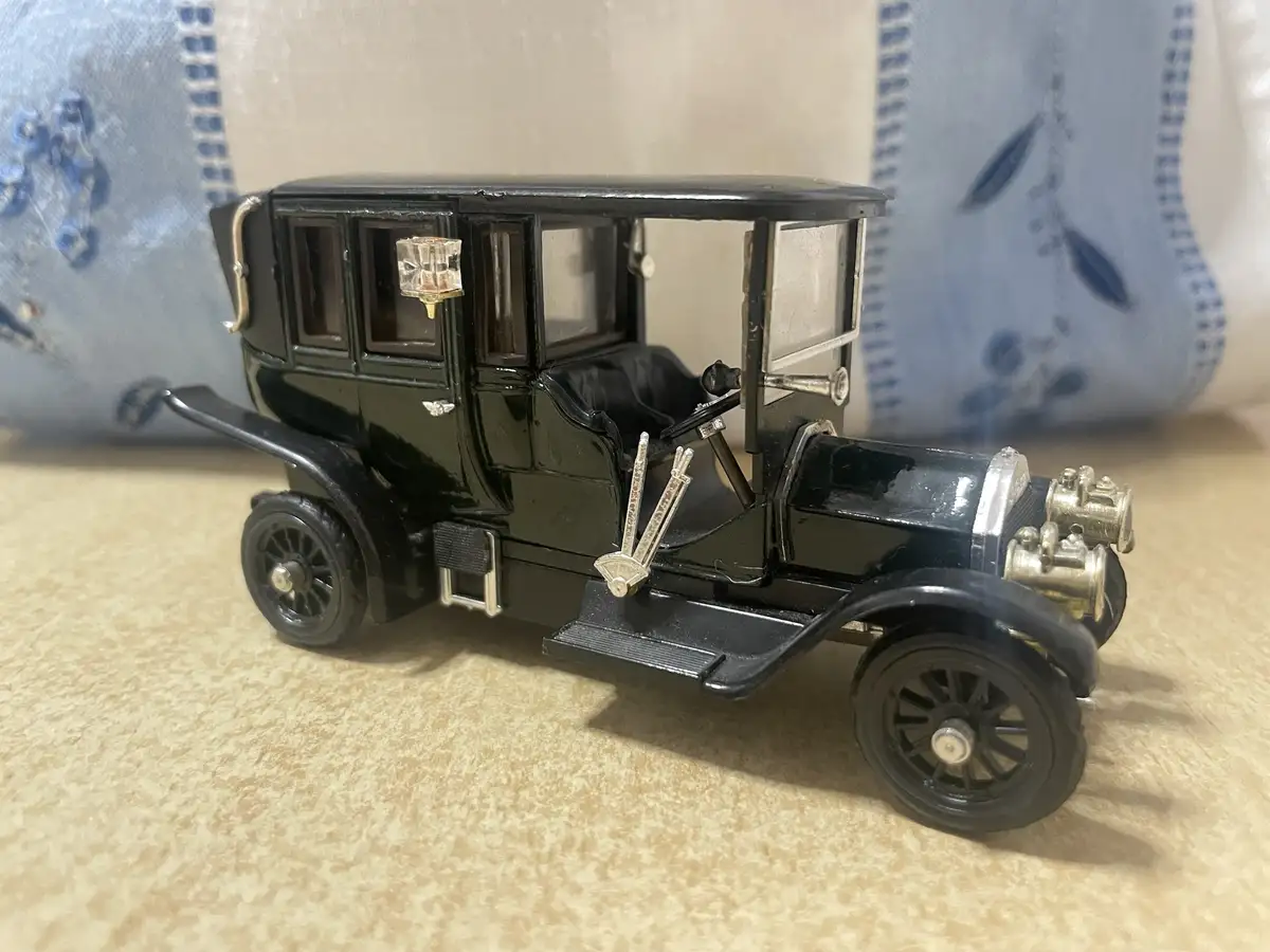 A black vintage toy car model with silver accents and spoked wheels sits on a beige textured surface, with a blue patterned…