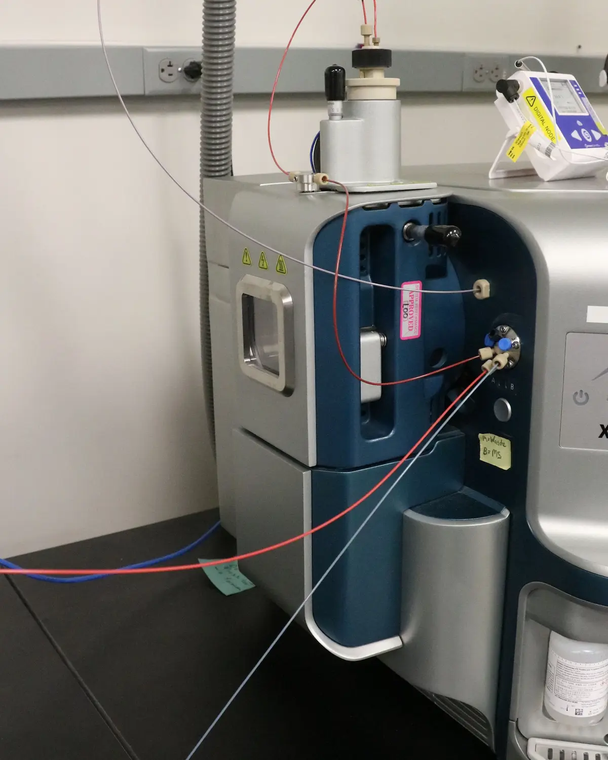 A close-up photo of a complex laboratory instrument, likely a liquid chromatograph, with multiple colored tubes connected to…