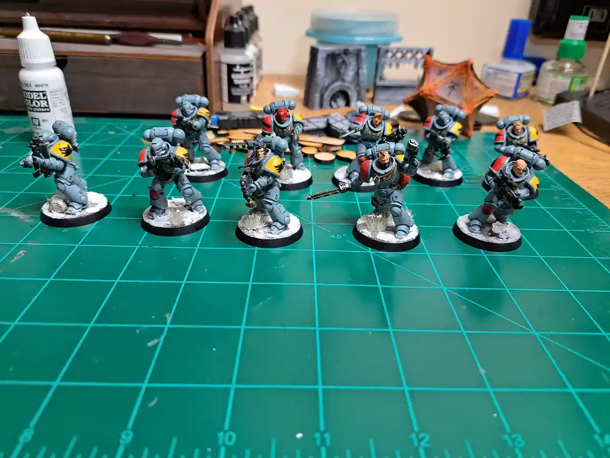 A collection of painted miniature sci-fi soldiers in grey armor with red and yellow accents stand on circular bases on a…