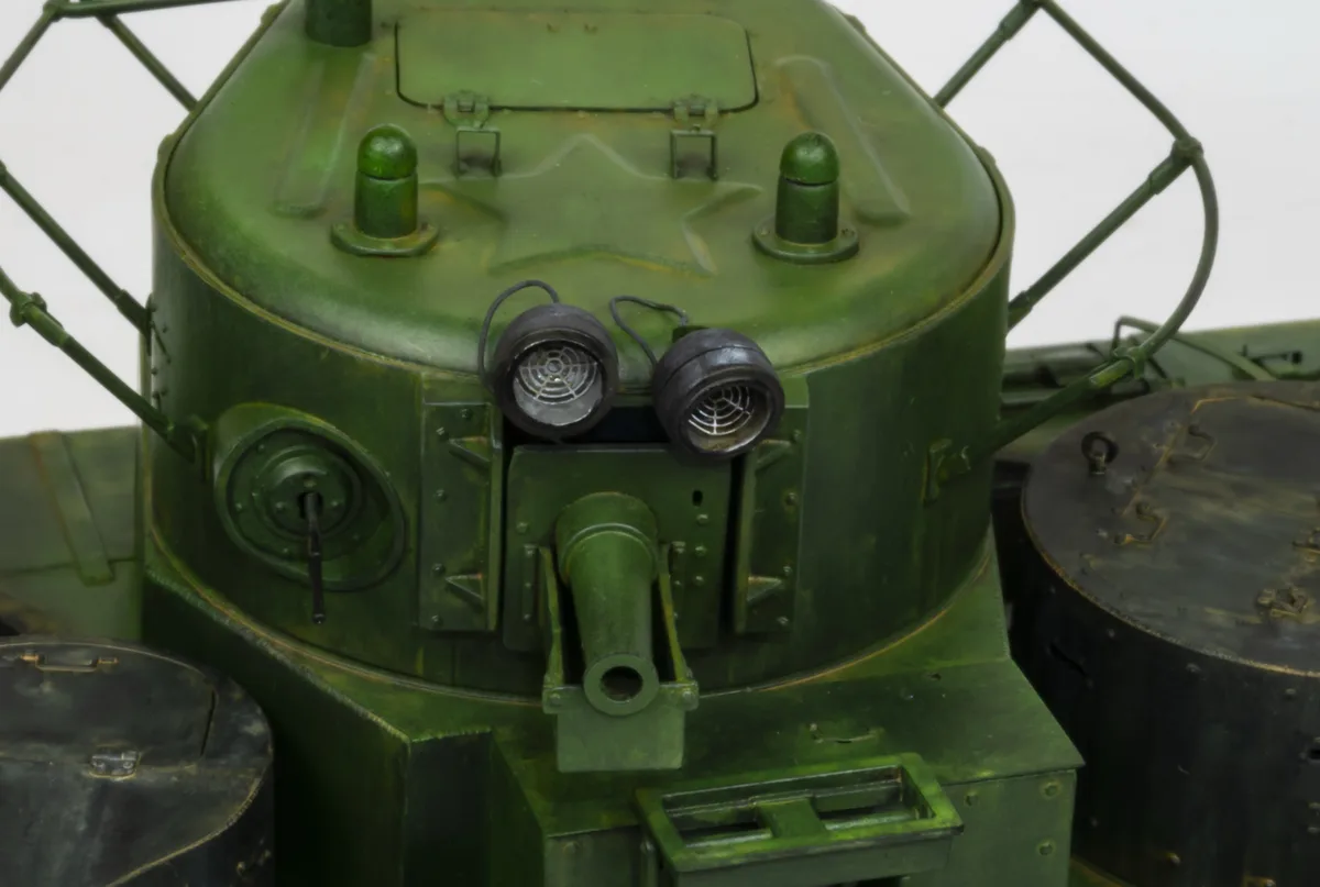 A close-up of a green military tank's turret, featuring two round headlights, a small cannon barrel, and a star-shaped…