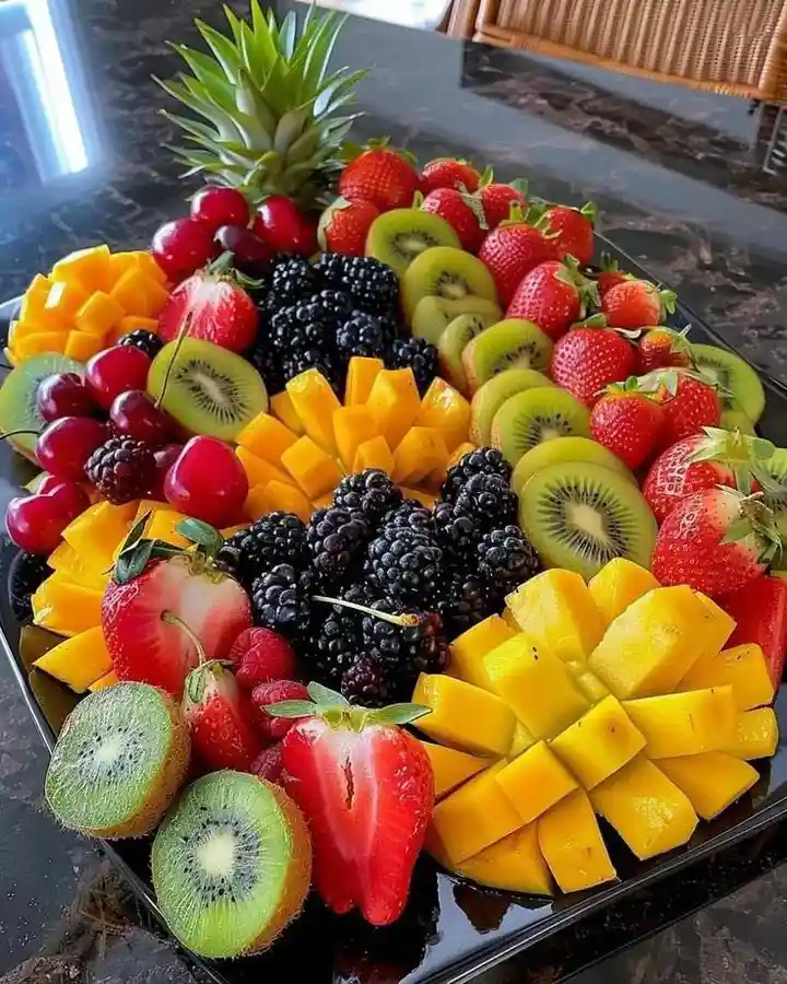 a vibrant, artfully arranged fruit platter on a black tray, featuring pineapple, strawberries, kiwis, blackberries…