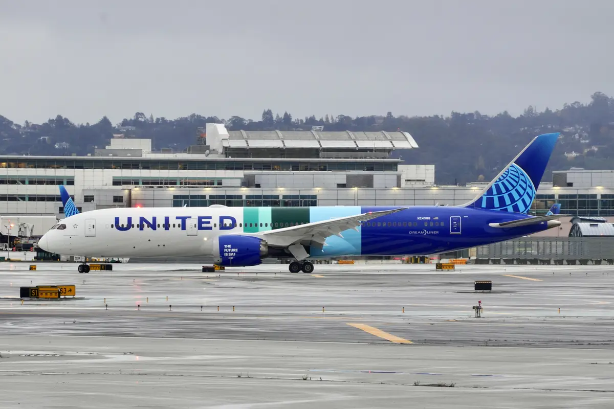 A United Airlines Boeing 787 Dreamliner is parked on a wet airport tarmac, with the text 'THE FUTURE IS SAF' visible on the…