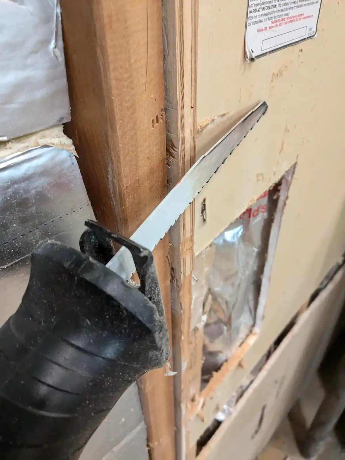 A close-up photo shows a reciprocating saw blade stuck at an awkward angle, wedged between a wooden stud and drywall in a…