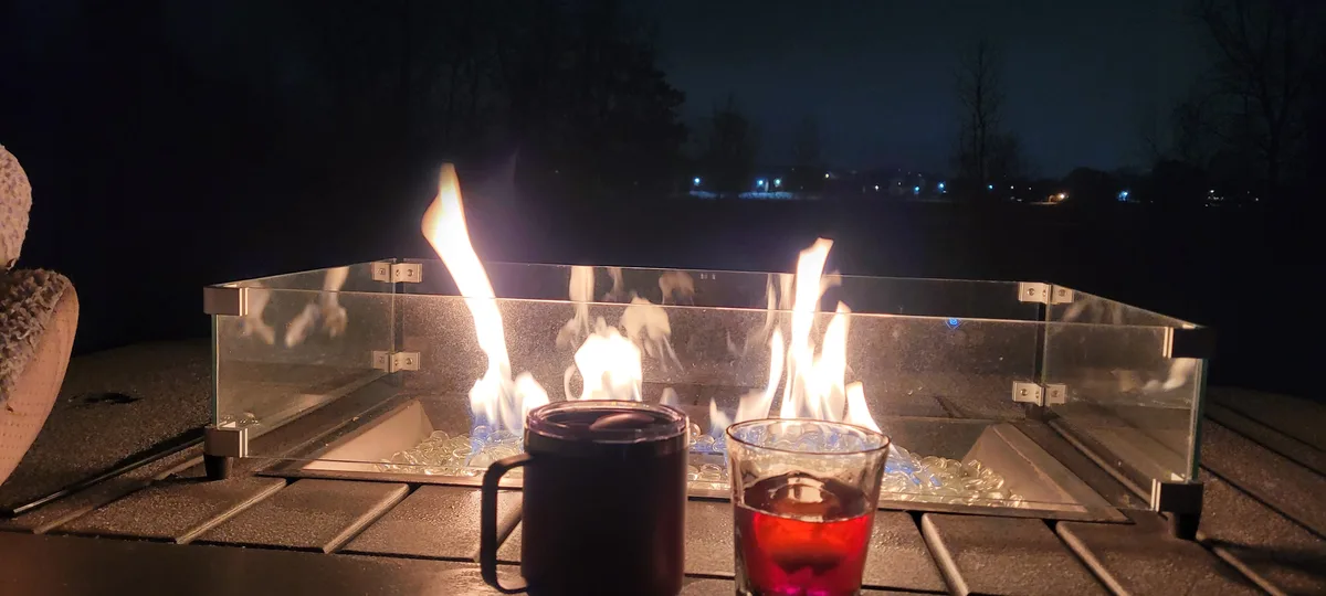 A nighttime photo shows two drinks — a dark mug and a glass with red liquid — placed in front of a modern glass-enclosed…