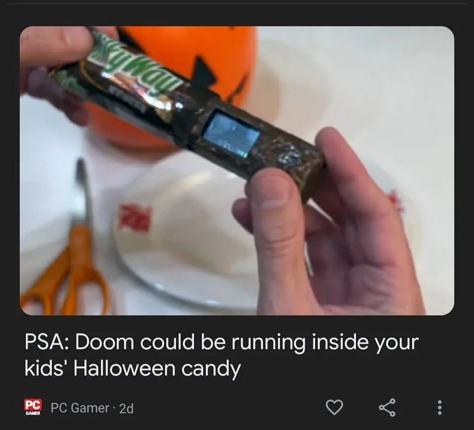 A person holds a wrapped Snickers bar that has been modified to look like a small, rugged handheld gaming device with a…