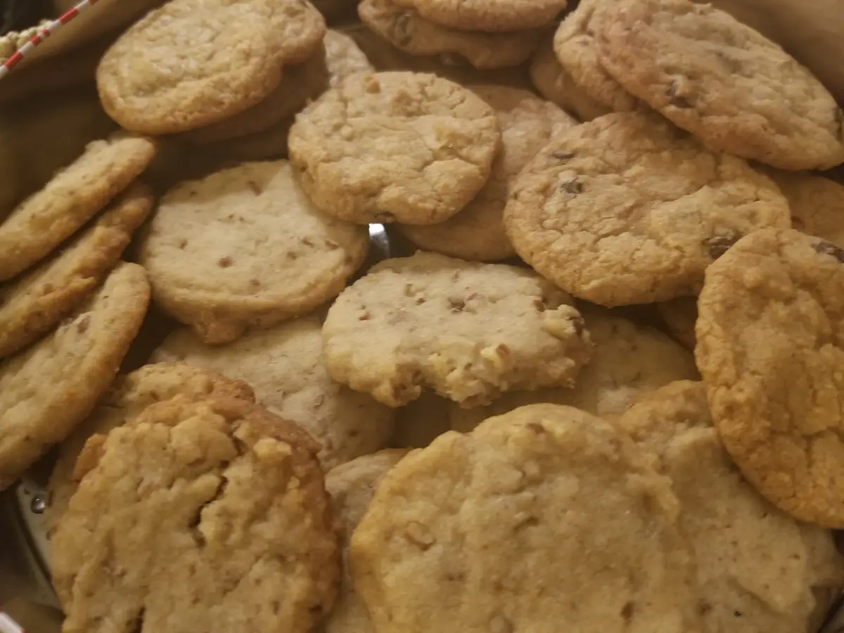 A close-up photo shows a pile of golden-brown, slightly crinkled cookies with visible chunks of nuts or chocolate. One…