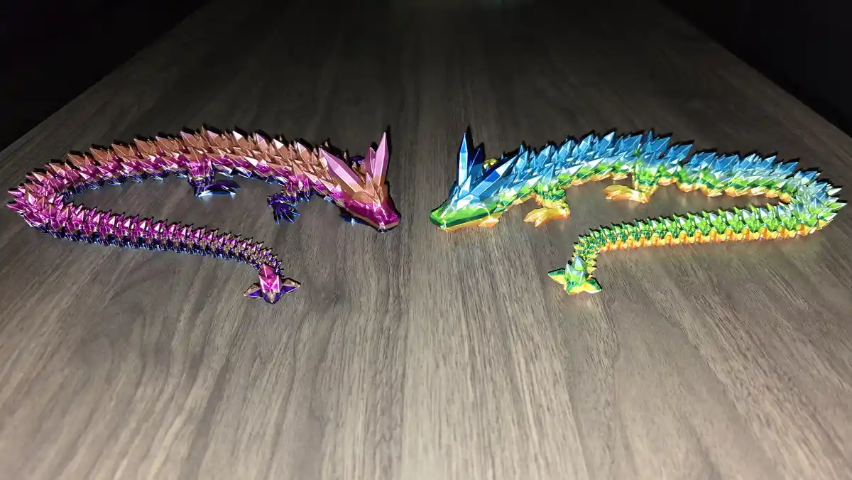 Two colorful origami dragons with iridescent, geometric scales lie on a dark wooden surface, facing each other. One dragon…