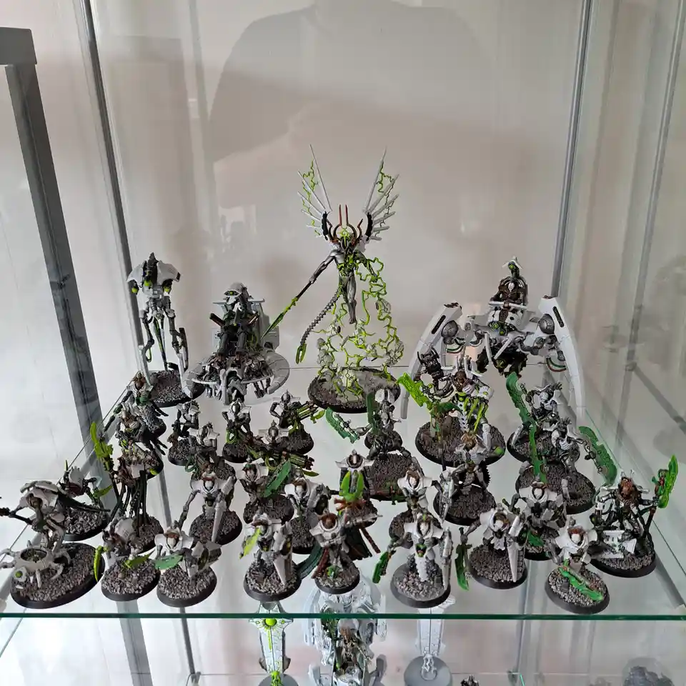 A glass display case holds a large collection of intricately painted miniature figurines, mostly white and green, resembling…