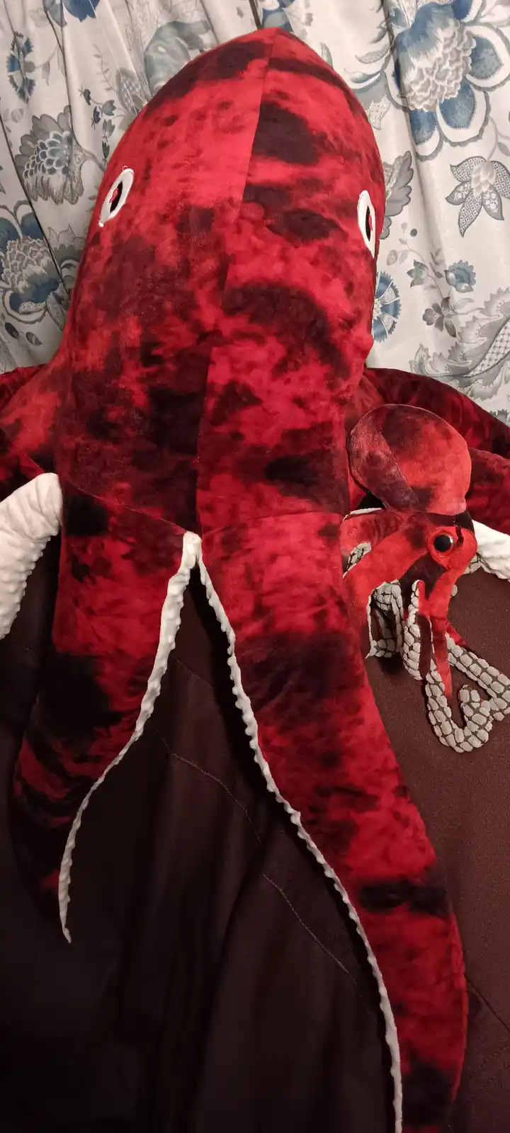 A large, red plush octopus toy with white trim on its tentacles is shown from the back, revealing its head and eyes. The toy…