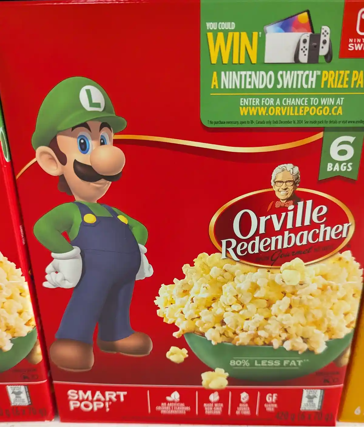 A red box of Orville Redenbacher's Smart Pop! popcorn features Luigi from Mario games standing beside a bowl of popcorn. The…