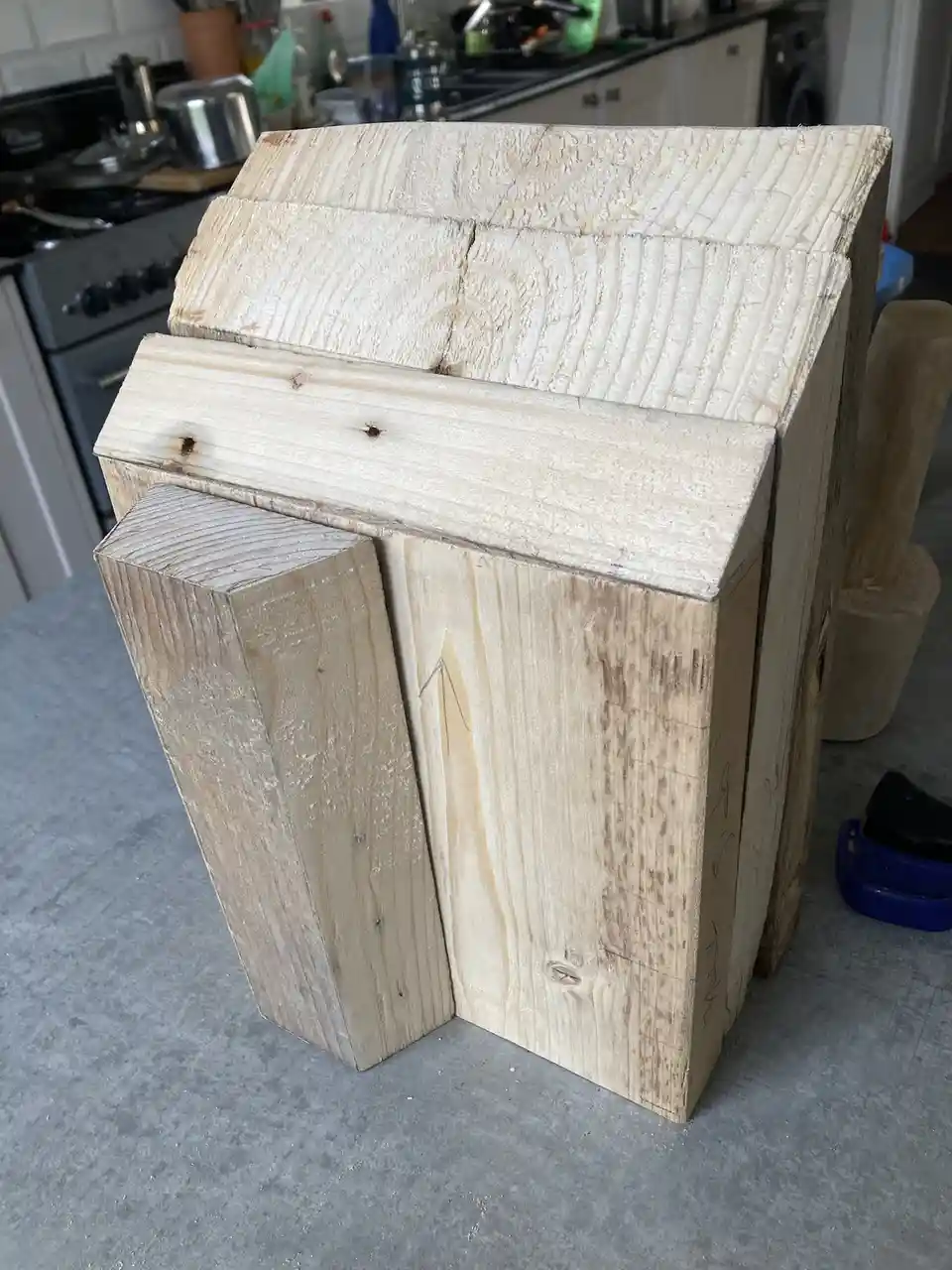 A large, rough-hewn wooden block, shaped like a knife block with a slanted top and a protruding rectangular section, sits on…