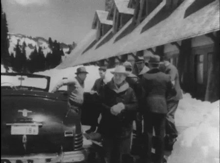 A black-and-white sequence shows a man in a hat getting out of a vintage car in snowy conditions near a lodge, followed by a…