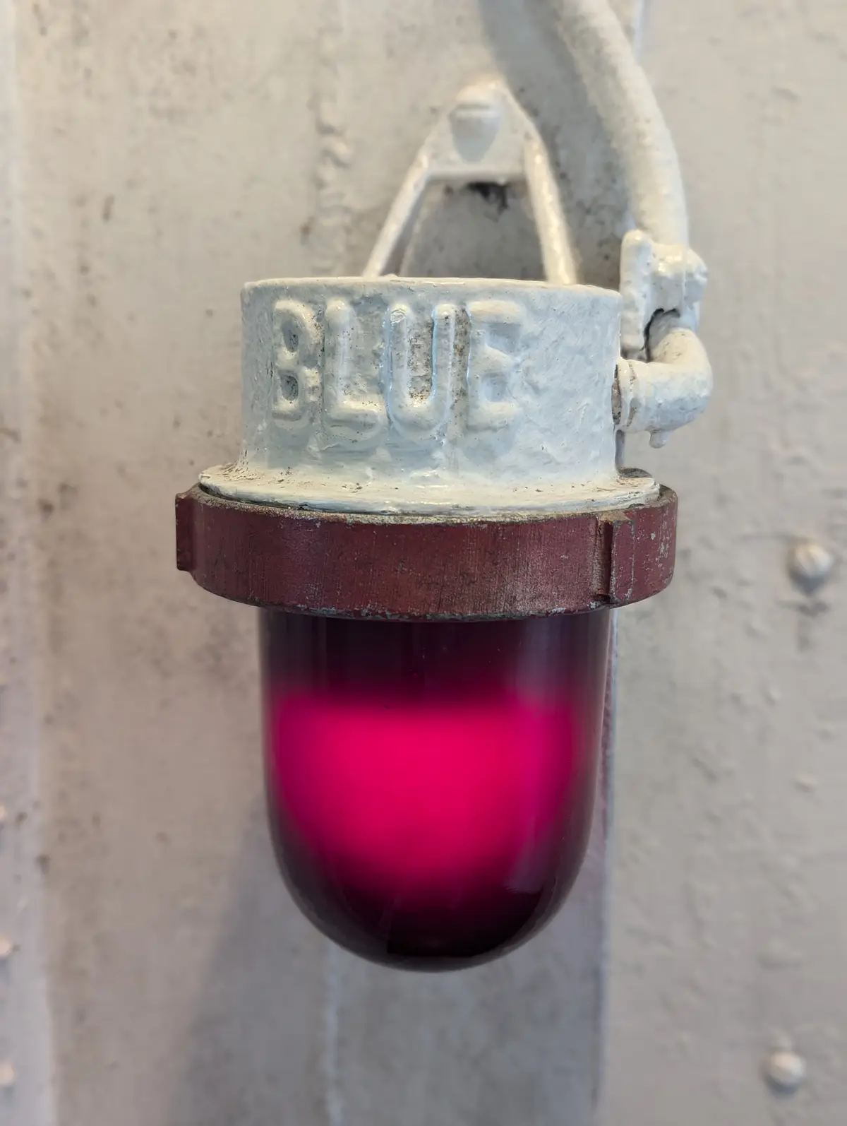 A close-up of an industrial-style signal light fixture mounted on a textured wall, with the word 'BLUE' embossed on its…