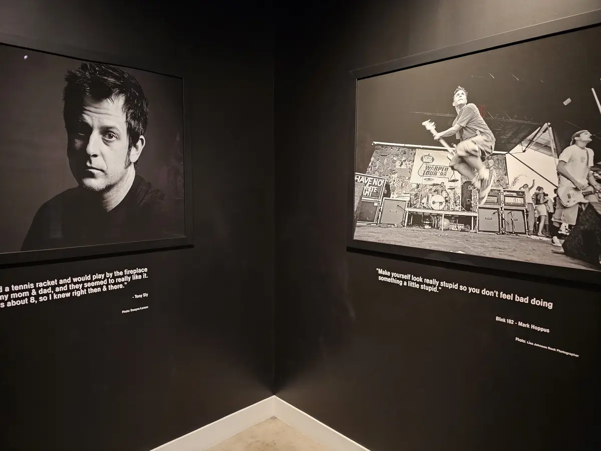 Two framed black-and-white photos hang on a dark wall in a museum corner. The left photo shows a man's portrait with a…