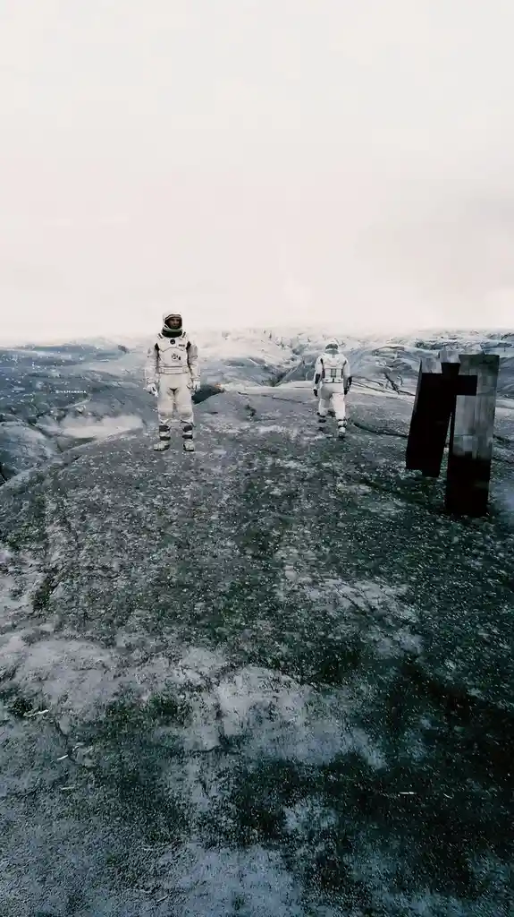 Two astronauts in white space suits stand on a rocky, icy landscape under a pale sky. One astronaut faces forward, while the…