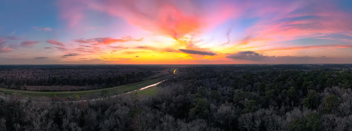 A panoramic aerial photo captures a stunning sunset over a vast forested landscape, with vibrant pink, orange, and yellow…