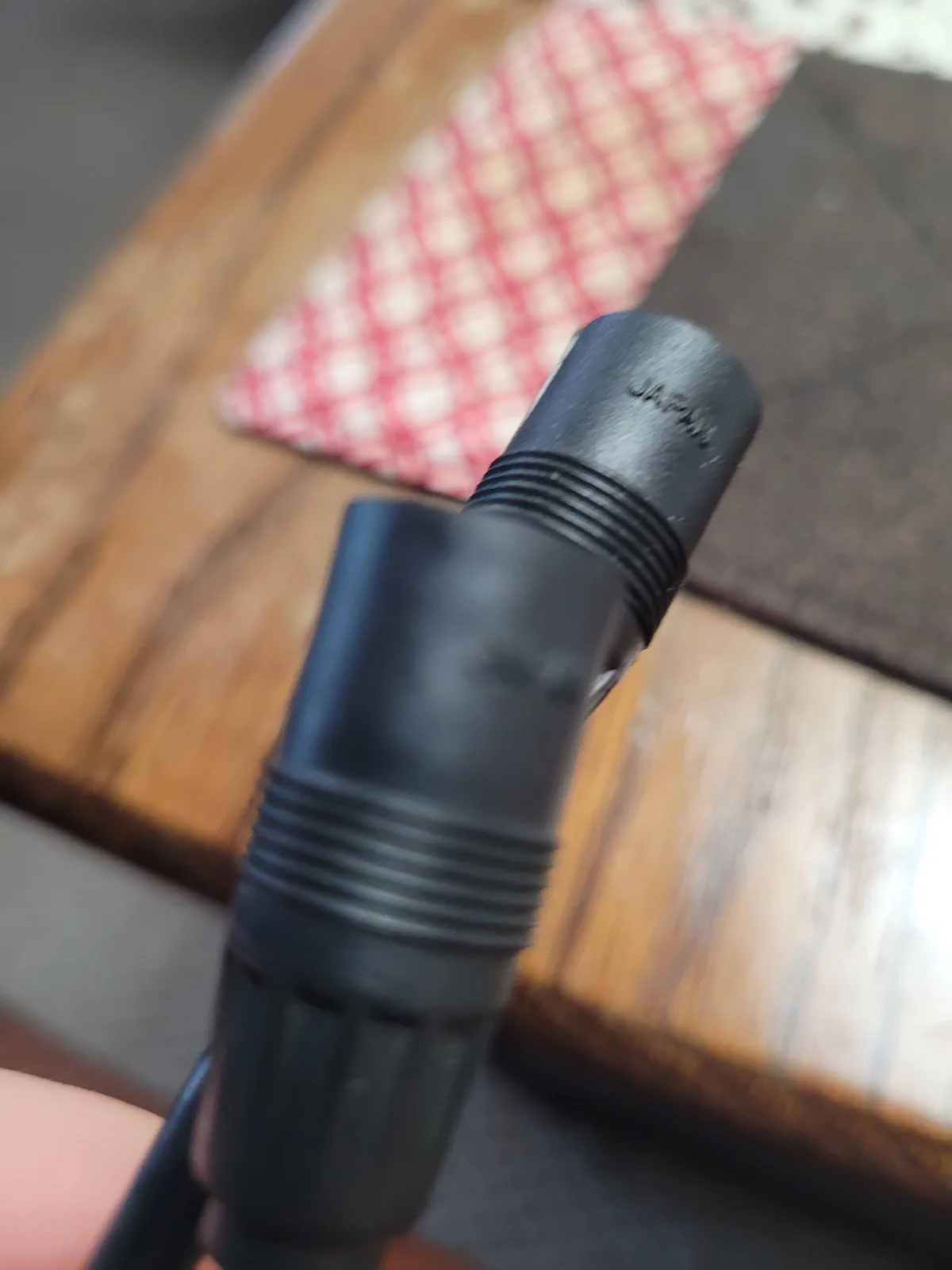 A close-up photo shows the end of a black, threaded electrical plug or connector being held by a person's thumb, with the…