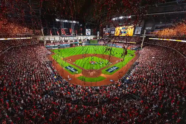 A wide-angle photo of a packed baseball stadium during a celebration, with red and gold confetti falling over the field and…