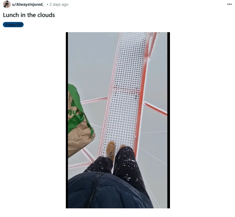 A first-person view of someone walking on a narrow, grated metal walkway covered in snow, holding a brown paper bag with…