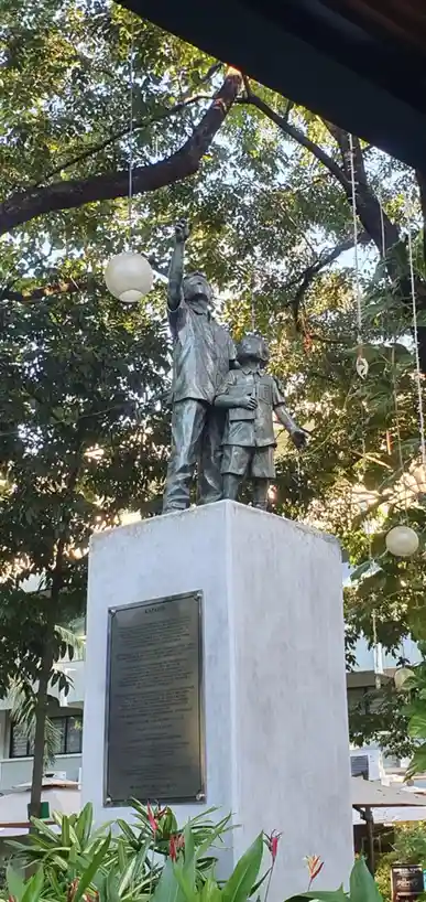 A bronze statue of two children, one pointing upward while the other stands beside them, mounted on a concrete pedestal with…