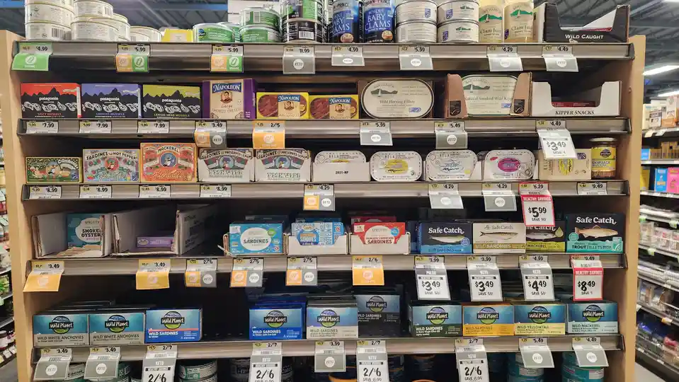 A grocery store aisle filled with various canned and packaged seafood products, including sardines, anchovies, mackerel, and…